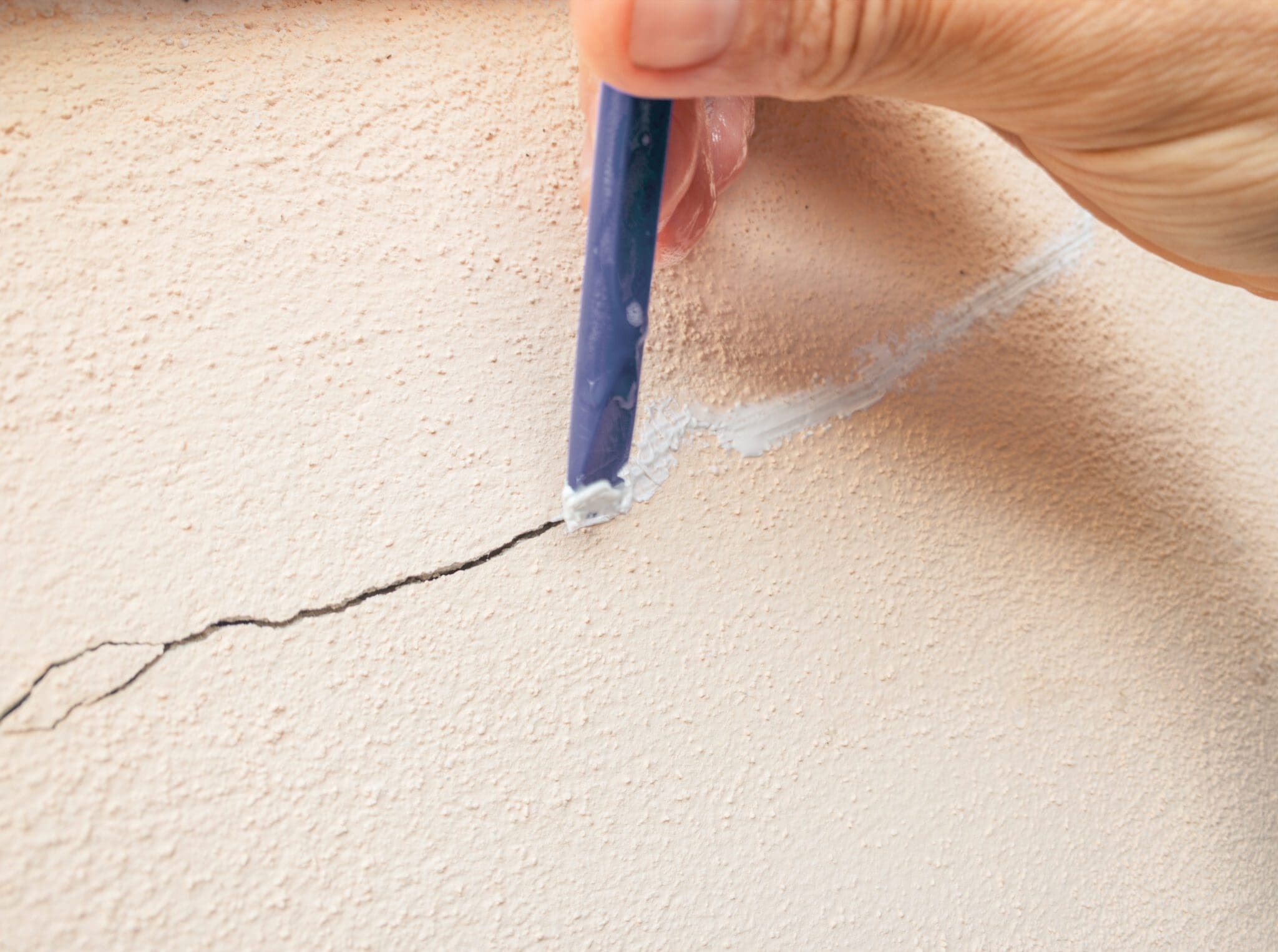 Hand filling a crack in the wall with white filler material.