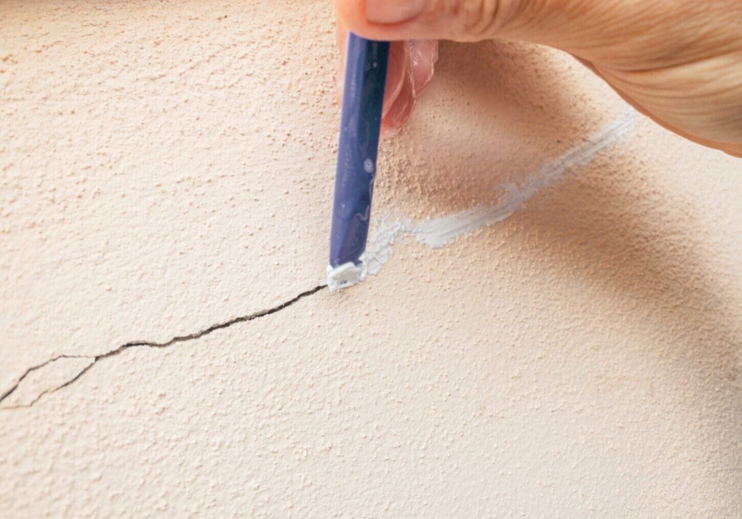 Hand filling a crack in the wall with white filler material.